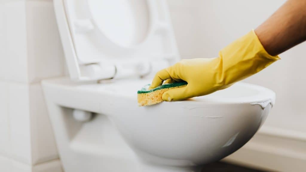 Hand met gele schoonmaakhandschoen poetst wc met zachte spons
