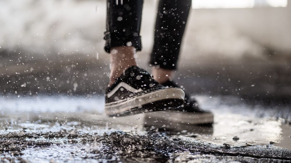 Iemand met Vans schoenen aan trapt in een kleine modderpoel