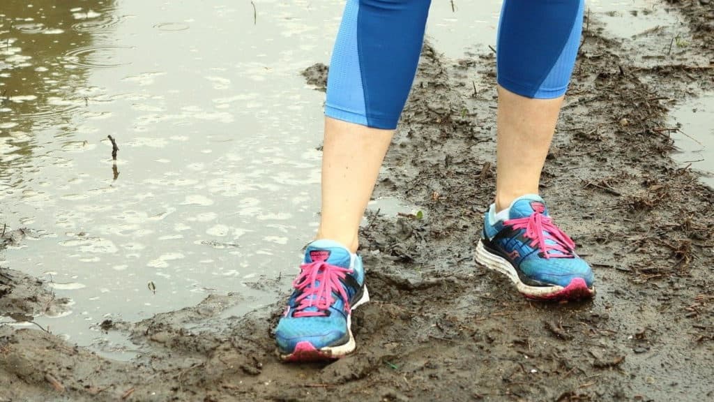 vrouw met hardloopschoenen staat in de modder