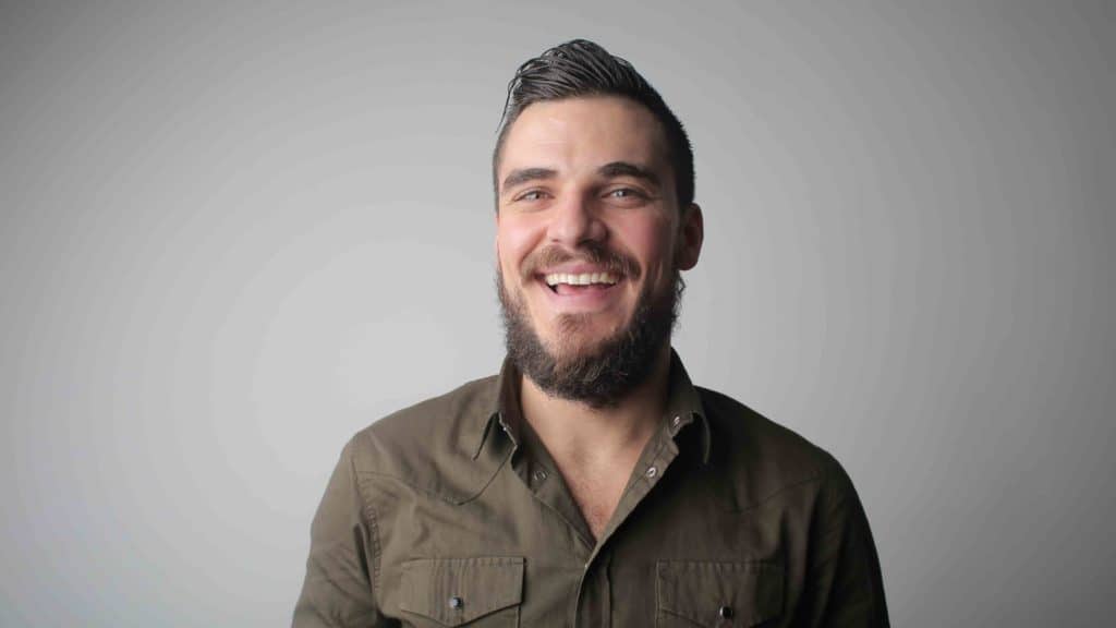 man met baard lacht voor een grijze achtergrond