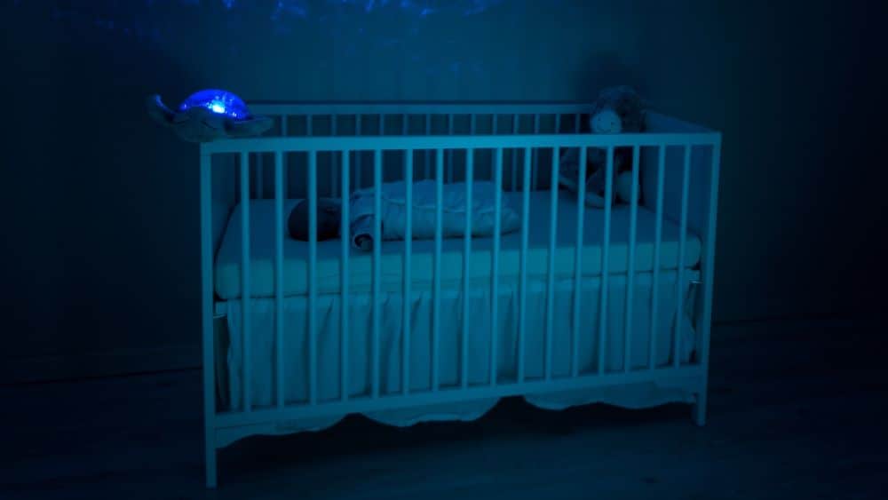 Baby slaapt in babybedje met blauwe lamp aan