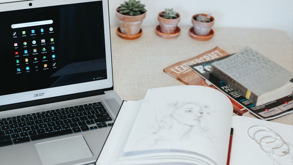 Chromebook op tafel met schetsboek ernaast en wat plantjes en boeken