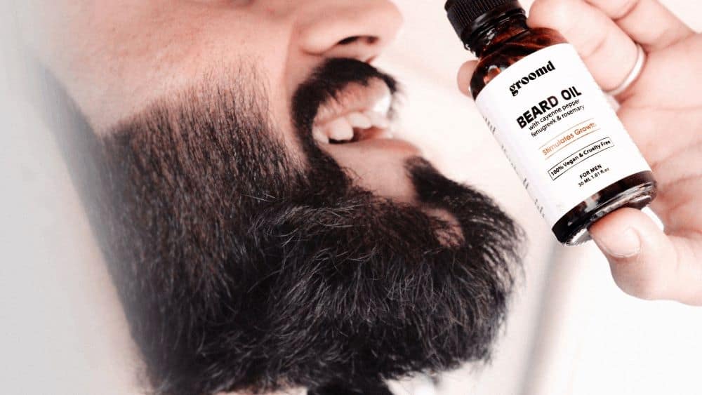 Lachende man met baard van zijkant die een flesje baardolie voor zijn gezicht houdt