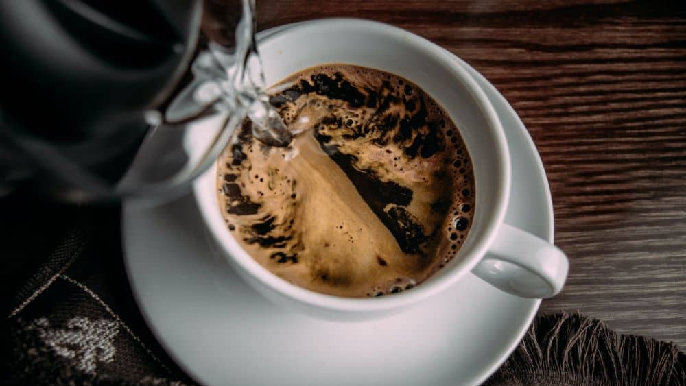 Water wordt in een wit kopje met koffie gegoten