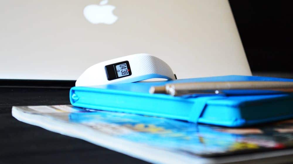 Witte activity tracker achter een macbook op een blauw boekje en tijdschrift