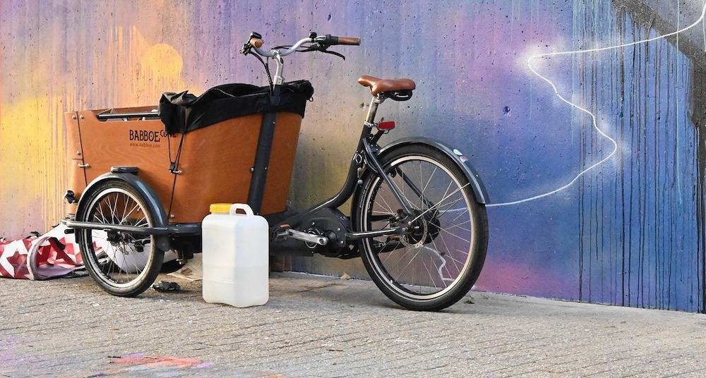 Een bakfiets tegen een muur met graffiti.