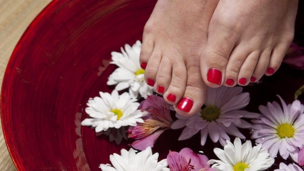 Voeten met gelakte rode nagels in een rode kom met water en bloemen