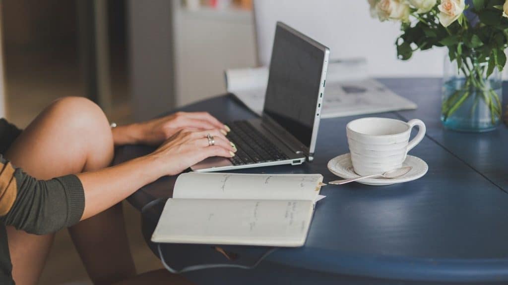 vrouw werkt aan tafel met laptop, notebook en kopje koffie