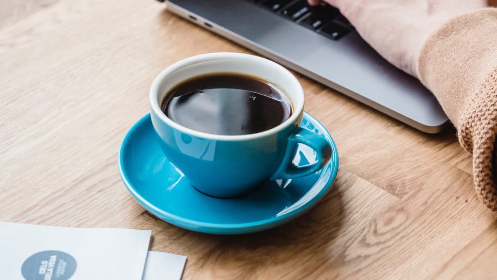kop koffie op houten tafel met werkend persoon op laptop