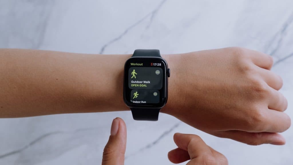 Blanke linkerarm met een smartwatch om. De hand is horizontaal gepositioneerd. Op het scherm is "outdoor walk, open goal" te zien. Een deel van de rechterhand is ook zichtbaar.