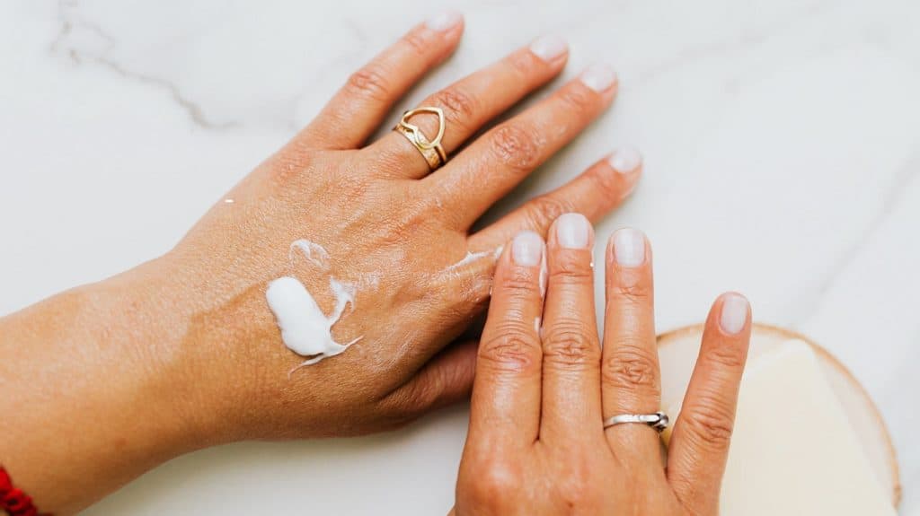 Twee blanke vrouwenhanden, met op de linkerhand een witte crème.