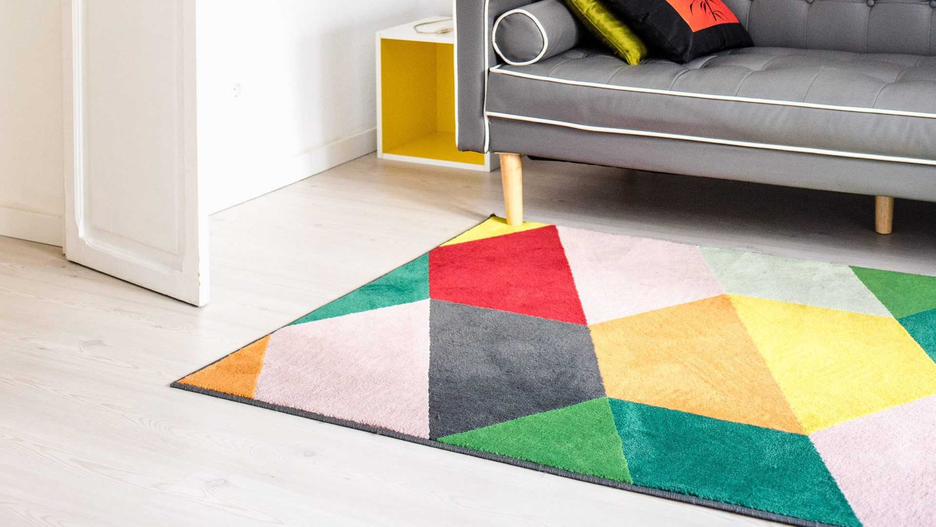 gekleurd tapijt op licht houten vloer in woonkamer met grijze bank