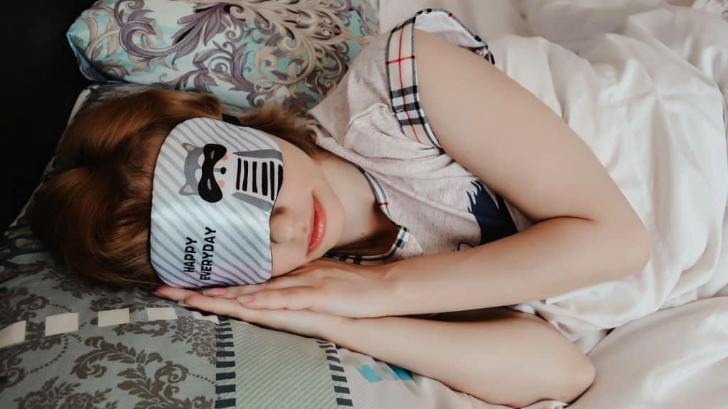 Roodharig meisje liggend op bed met een slaapmasker die haar ogen bedekt met de tekst "happy everyday"