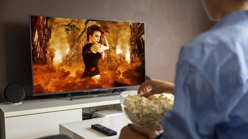 man met popcorn op schoot kijkt naar film op tv