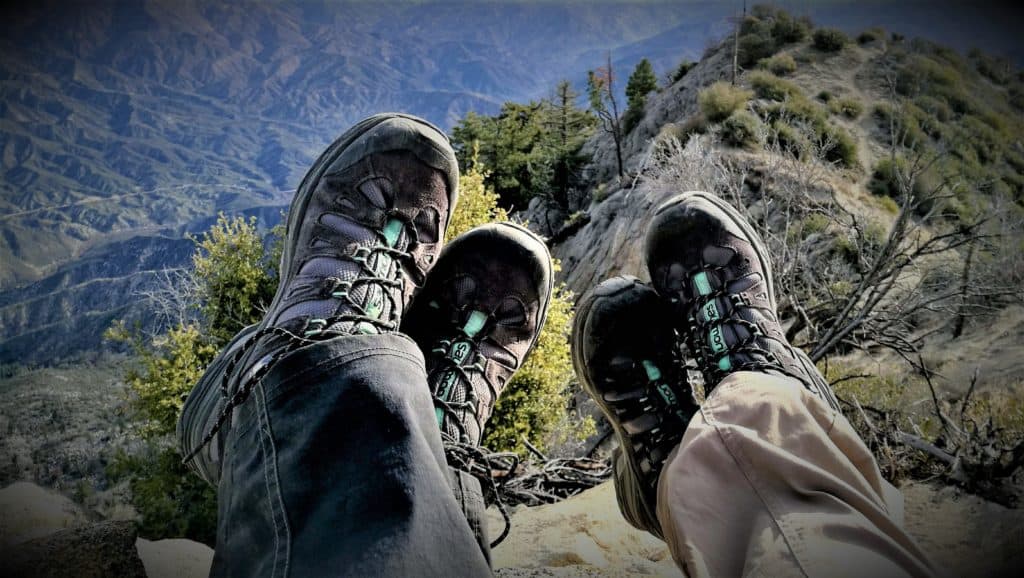 Twee paar benen, met wandelschoenen die boven een berg bungelen.