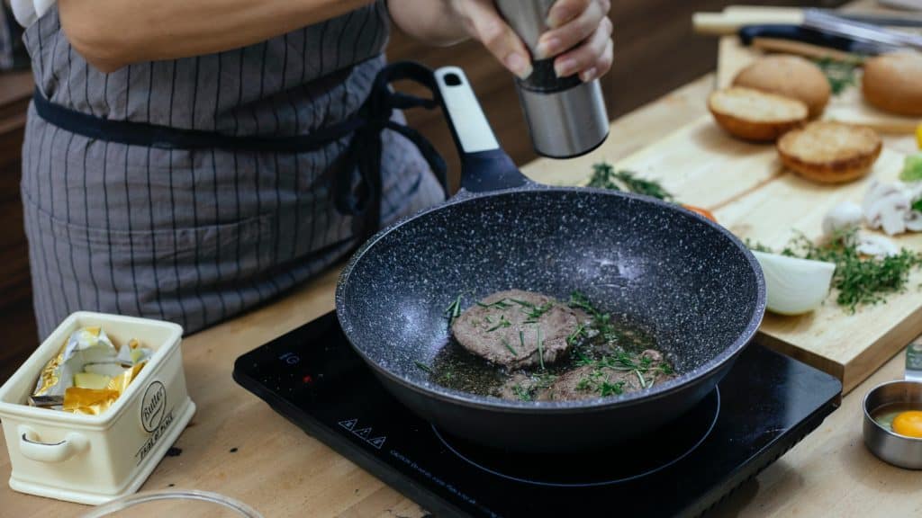 Wokpan met daarin vlees op een inductiekookplaat.