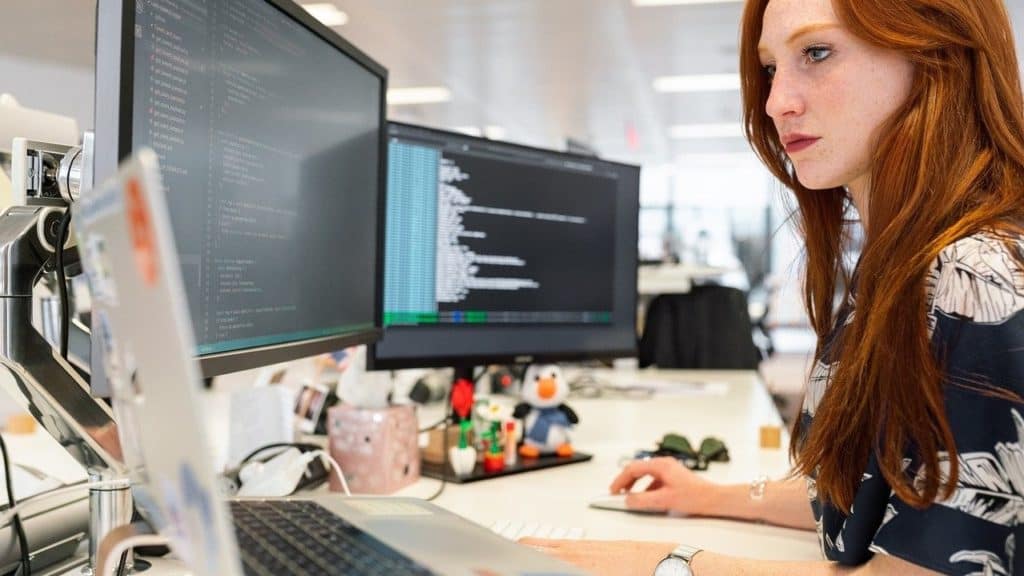 vrouw werkt op twee monitoren en laptop