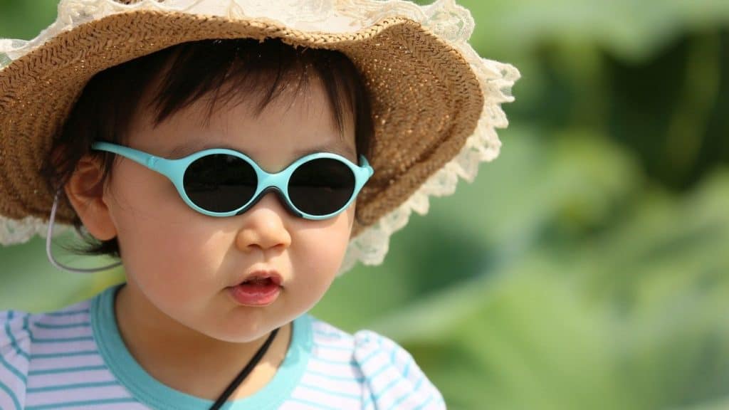 kind is buiten in de zon met hoed en bril op