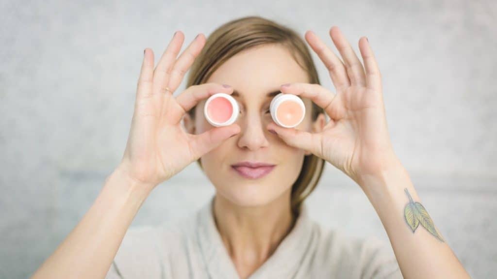 vrouw met twee gekleurde lippenbalsem potjes voor haar ogen