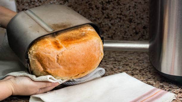 Vers bereid brood glijdt uit bakblik van een broodbakmachine