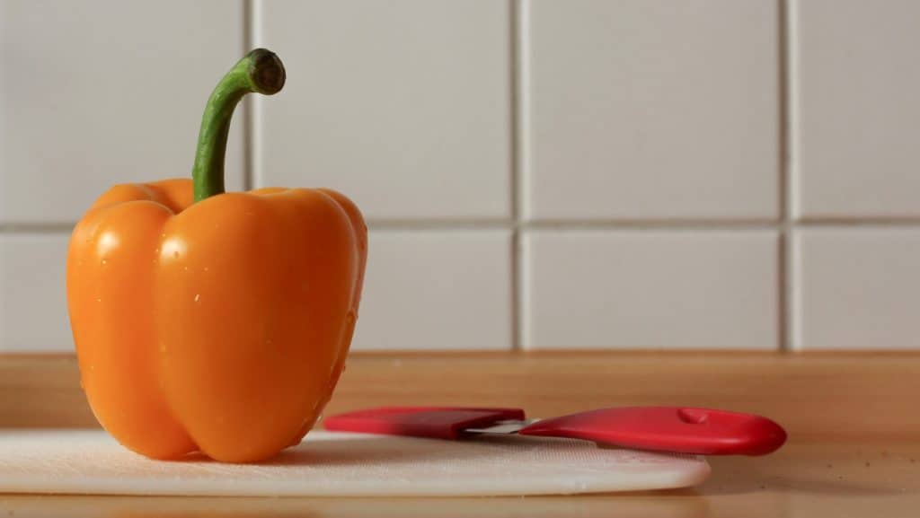gele paprika staat op een klein wit snijplankje met een rood mes ernaast