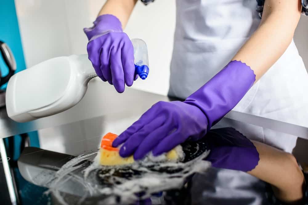 vrouw maakt elektrisch fornuis schoon met spons en schoonmaak middel met paarse handschoenen