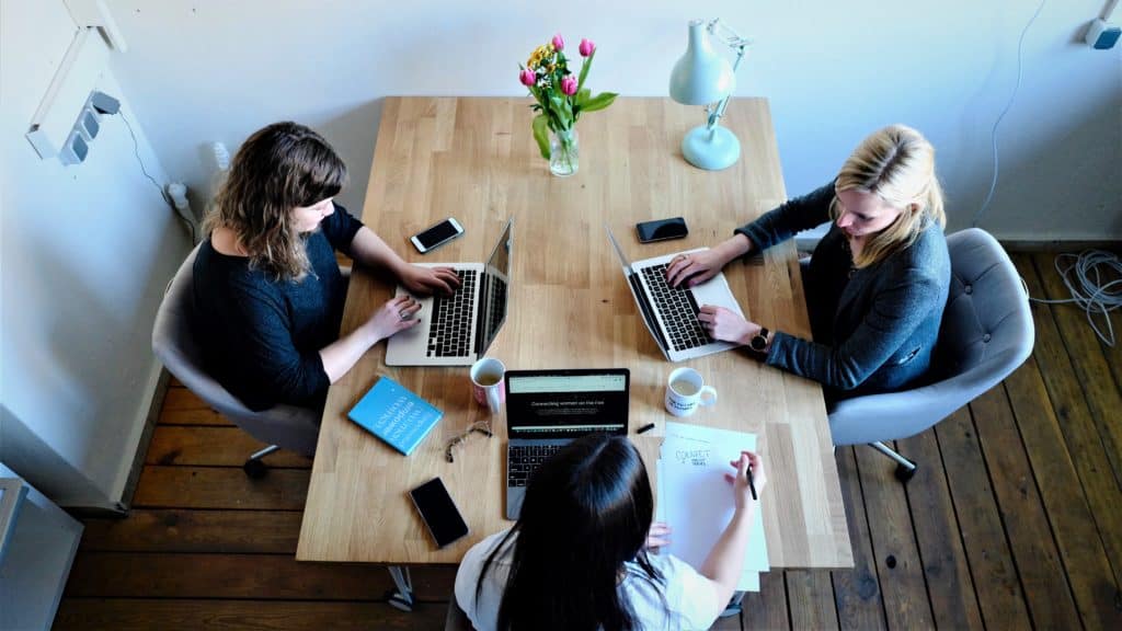 Drie vrouwen met laptops open die rond een tafel zitten. 