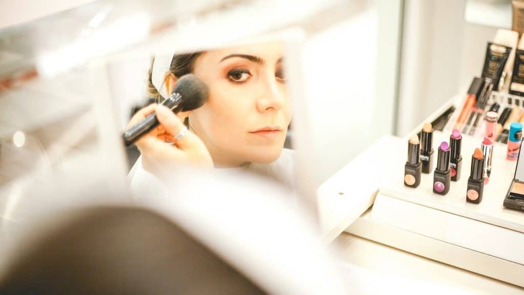 Vrouw kijkt in kleine spiegel tijdens het opbrengen van make-up