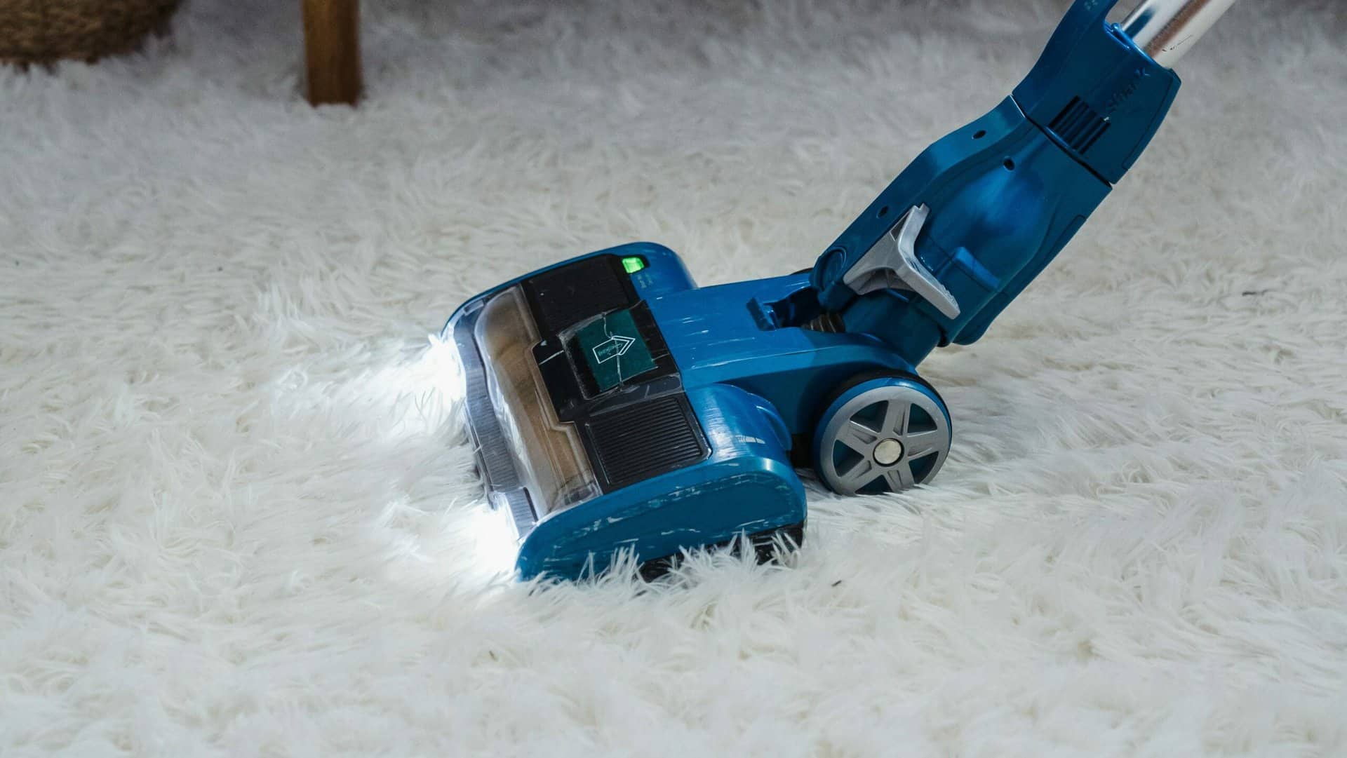 blauwe snoerloze stofzuiger op hoogpolig tapijt met led verlichting